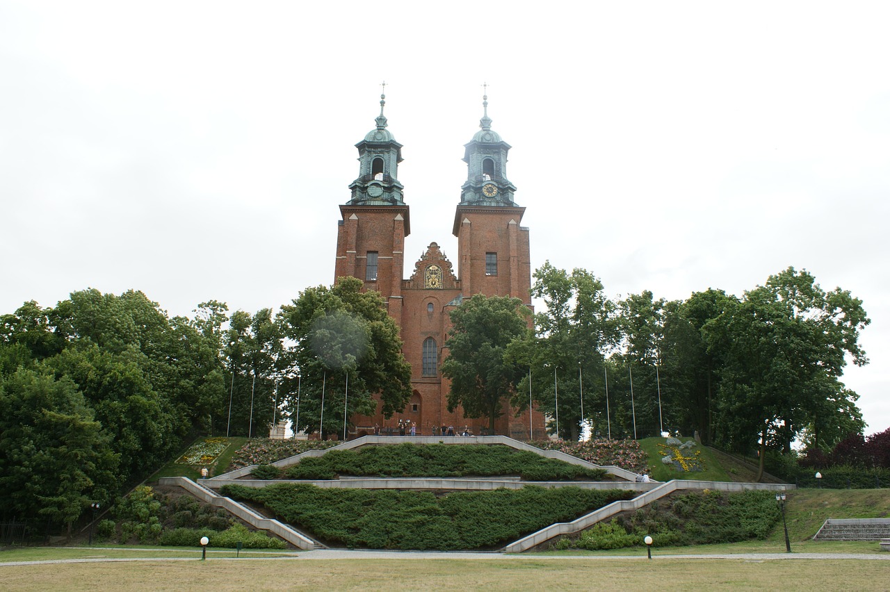 Przód Katedry Gnieźnieńskiej na niewielkim wzniesieniu w otoczeniu zieleni